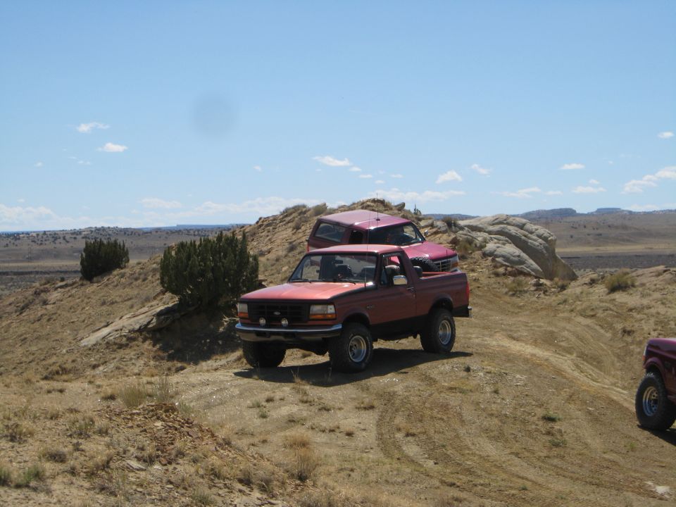 Red 1993 Ford Bronco parked on a dirt hill with a pink Ford Bronco behind it