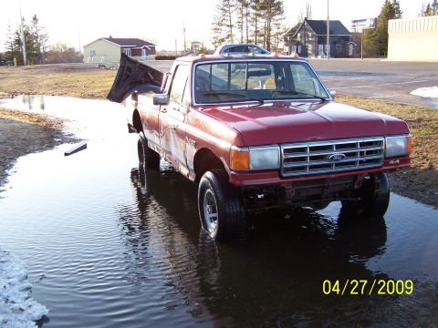 1989 Ford F-150 - A red pickup truck sits in a large puddle with its hood open, reflecting the sky.