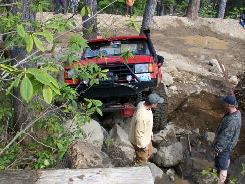 1989 Ford Bronco - A red off-road vehicle maneuvers through a rocky terrain with two men observing.