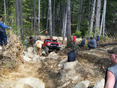 1989 Ford Bronco - A red 1989 Ford Bronco tackles a challenging rocky trail with onlookers observing the off-road adventure.