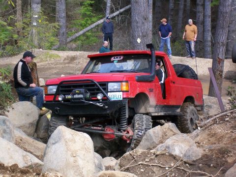 1989 Ford Bronco - A red off-road vehicle tackles a challenging rocky trail with several onlookers observing the action.