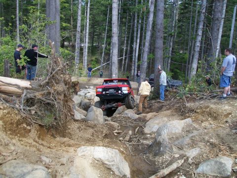 1989 Ford Bronco - Off-road enthusiasts watch a red 1989 Ford Bronco navigate a challenging rocky obstacle.