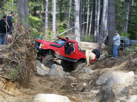 1989 Ford Bronco - A red off-road truck navigates a challenging rocky trail with spectators observing the action.