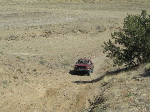 1993 Ford Bronco - A red pickup truck navigates a dirt road through a barren, hilly terrain under a clear sky.