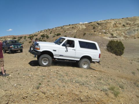 1993 Ford Bronco - Two Ford Broncos navigate a dusty, off-road trail under a clear blue sky.
