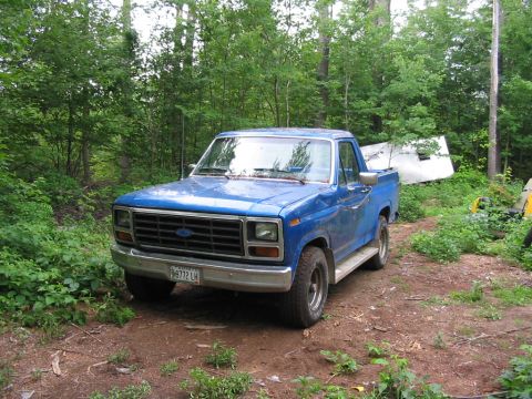 1985 Ford Bronco - A blue pickup truck sits in a wooded area, its front end angled towards the viewer.