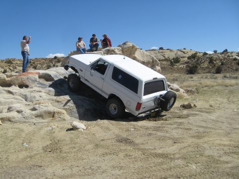 1993 Ford Bronco - A white 1993 Ford Bronco navigates a challenging rocky obstacle course under a clear blue sky.