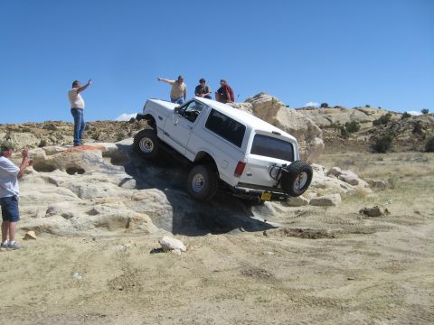 1993 Ford Bronco - White 1993 Ford Bronco navigating a rocky off-road trail with spectators.