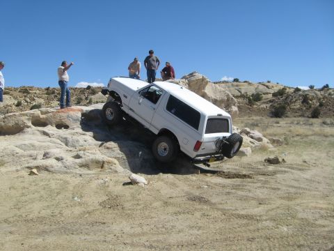 1993 Ford Bronco - White Ford Bronco navigates rocky terrain with onlookers observing the off-road maneuver.