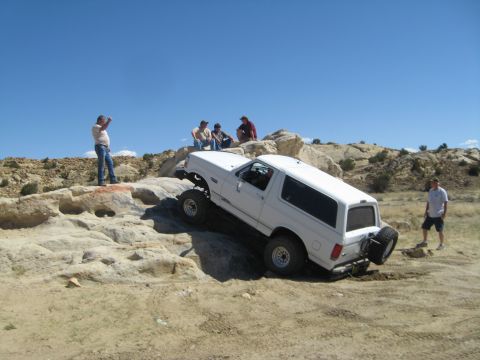 1993 Ford Bronco - A white 1993 Ford Bronco navigates a challenging rocky off-road course under a clear blue sky.