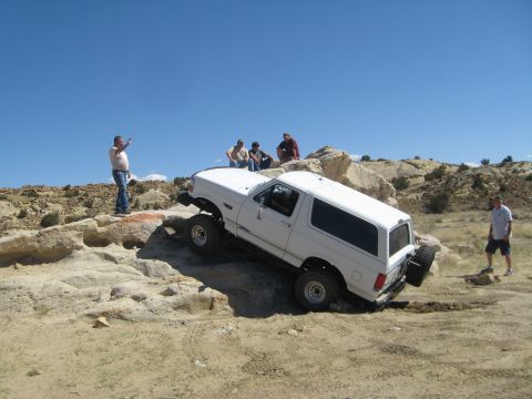 1993 Ford Bronco - A white 1993 Ford Bronco is shown off-roading on a rocky trail with several people observing the action.