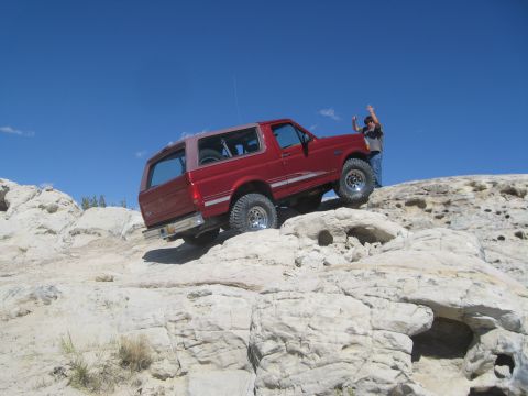 1993 Ford Bronco - A red 1993 Ford Bronco navigates a rocky off-road trail under a clear blue sky.