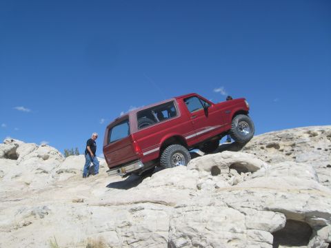 1993 Ford Bronco - Red 1993 Ford Bronco navigating a rocky trail under a clear blue sky.