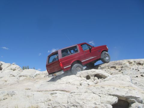 1993 Ford Bronco - This red SUV is navigating a challenging off-road course on a bright, sunny day.