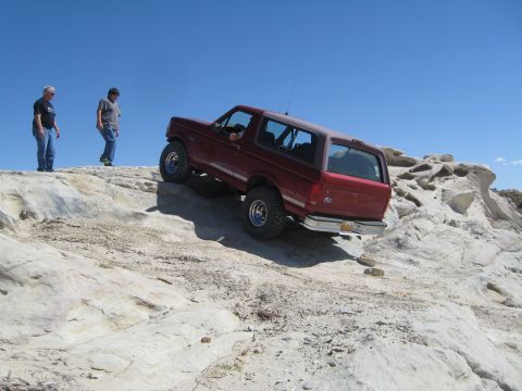1993 Ford Bronco - A red SUV navigates a steep, rocky incline under a clear blue sky.