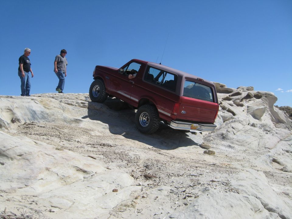 Red SUV climbing rocky terrain, two men watch from above