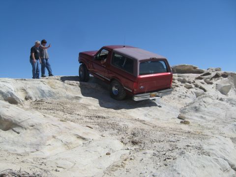 1993 Ford Bronco - A red 1993 Ford Bronco navigates a challenging rocky trail under a clear blue sky.