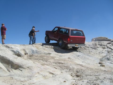 1993 Ford Bronco - A red 1993 Ford Bronco navigates a rocky off-road trail under a clear blue sky.