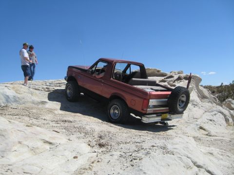 1993 Ford Bronco - A red Ford Bronco navigates a rocky trail under a clear blue sky.