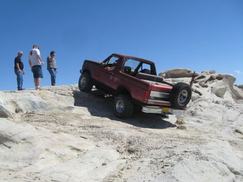 1993 Ford Bronco - A red Ford Bronco navigates a challenging rocky terrain under a clear blue sky.