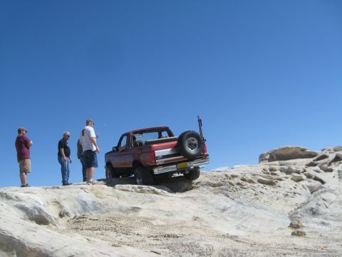 1993 Ford Bronco - A 1993 Ford Bronco navigates a rocky off-road trail under a clear blue sky.