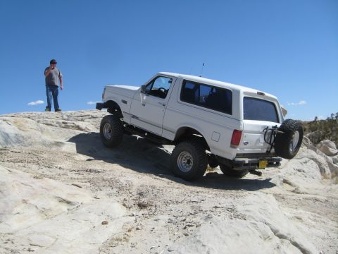 1993 Ford Bronco - White 1993 Ford Bronco navigating a rocky off-road trail under a clear blue sky.