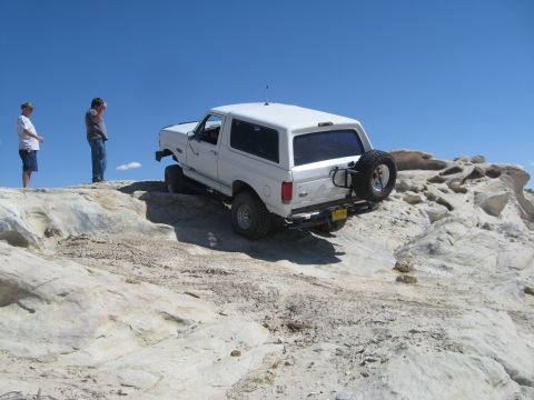 1993 Ford Bronco - A white SUV navigates a steep, rocky path under a clear blue sky.