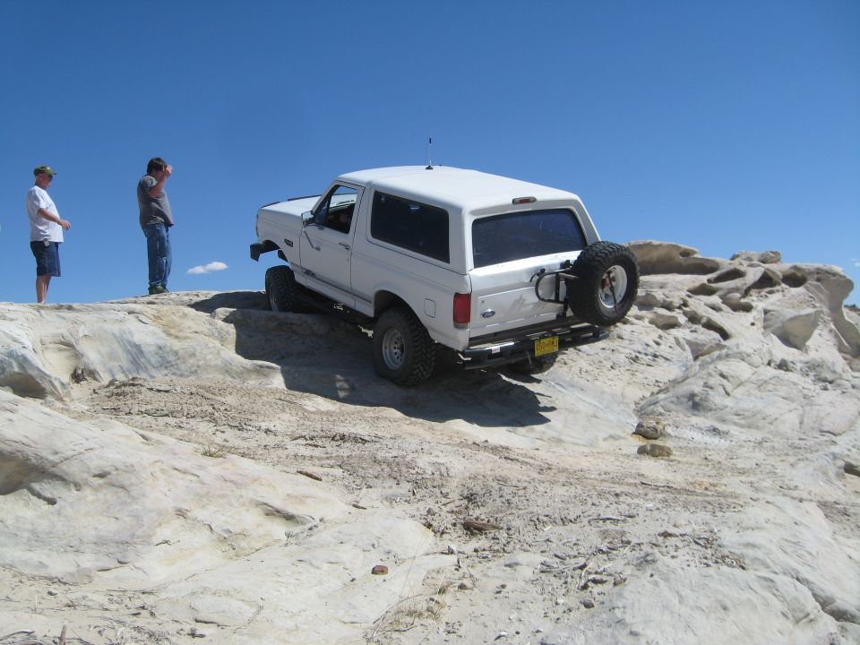 White SUV on a rocky incline with two people watching