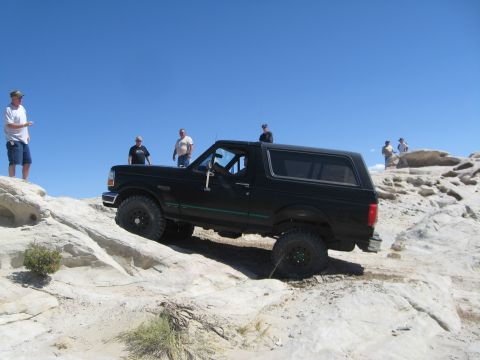 1993 Ford Bronco - A black Ford Bronco navigates a challenging off-road course with several onlookers present.
