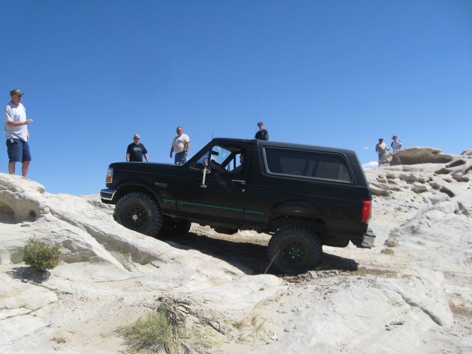 Black Ford Bronco climbing rocky terrain under a clear blue sky