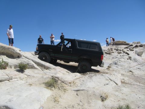 1993 Ford Bronco - A black 1993 Ford Bronco navigates a rocky off-road trail under a clear blue sky.
