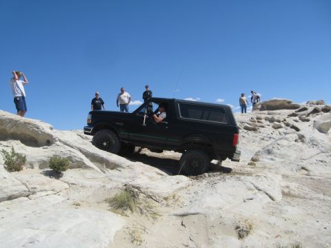 1993 Ford Bronco - A 1993 Ford Bronco navigates a rocky off-road trail under a clear blue sky.