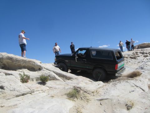 1993 Ford Bronco - A group of people watch as a black Ford Bronco navigates a rocky off-road trail under a clear blue sky.