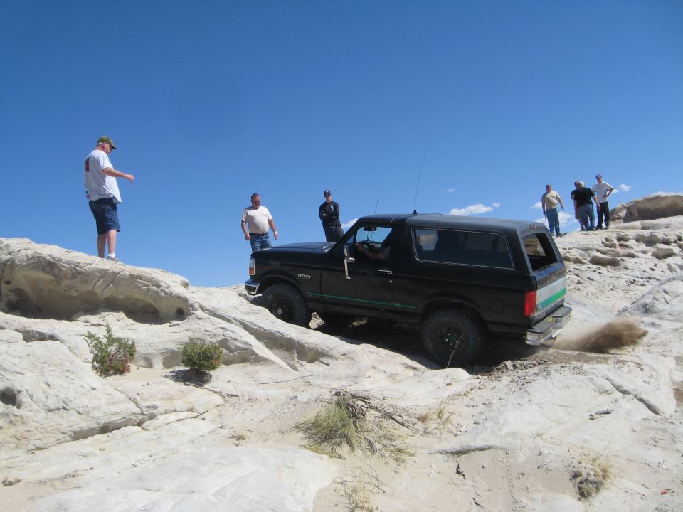 Black 1993 Ford Bronco climbing rocky terrain with people watching