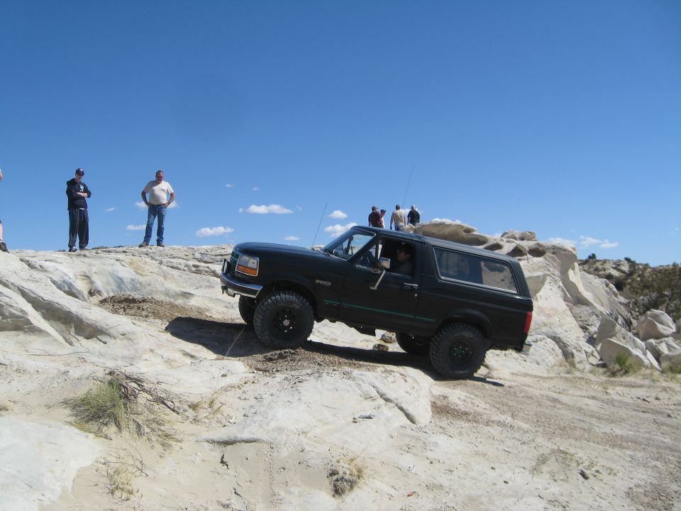 Black 1992 Ford Bronco climbing a rocky incline under a clear blue sky