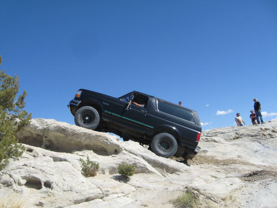 Black 1993 Ford Bronco climbing a rocky incline under a clear blue sky