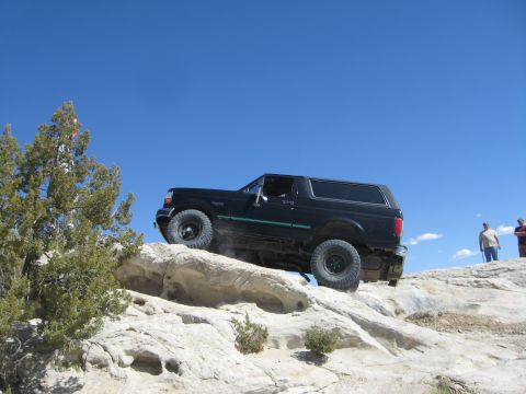 1993 Ford Bronco - A black Ford Bronco navigates a rocky off-road trail under a clear blue sky.