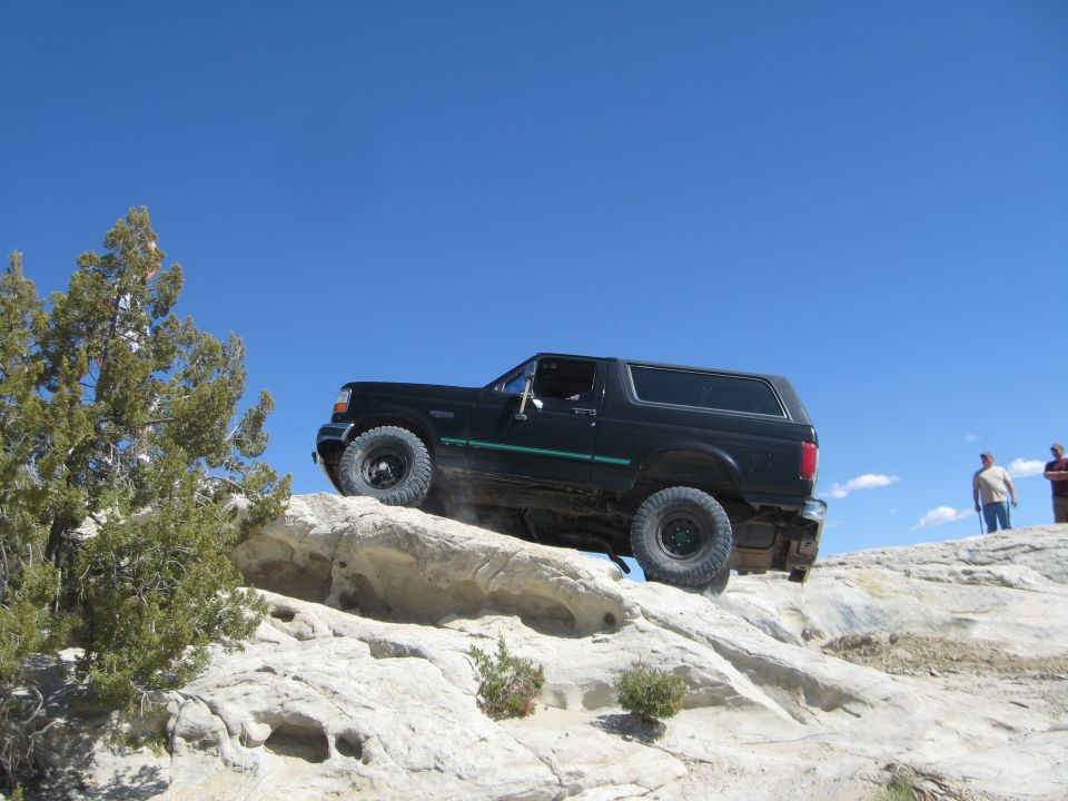 Black Ford Bronco climbing over rocks on a trail with two people watching