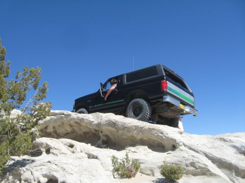 1993 Ford Bronco - A black Ford Bronco navigates a challenging rocky terrain on a bright, clear day.