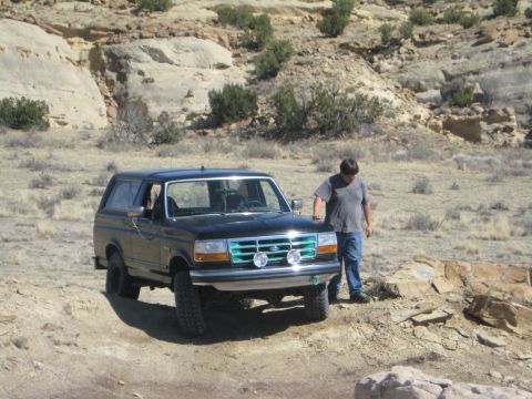 1993 Ford Bronco - A black 1993 Ford Bronco is parked on a dirt trail with a man standing beside it.