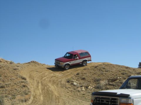 1993 Ford Bronco - Two vehicles navigate a dusty, off-road trail under a clear blue sky.