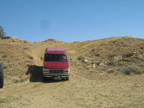 1993 Ford Bronco - A red van navigates a sandy incline, with its grille suggesting a 1993 model year.