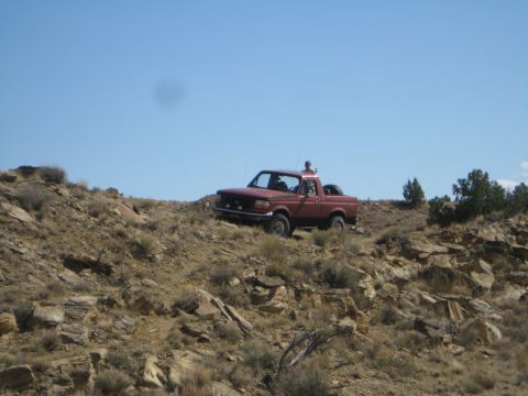 1993 Ford Bronco - A red pickup truck navigates a , off-road terrain with sparse vegetation and rocky outcrops.