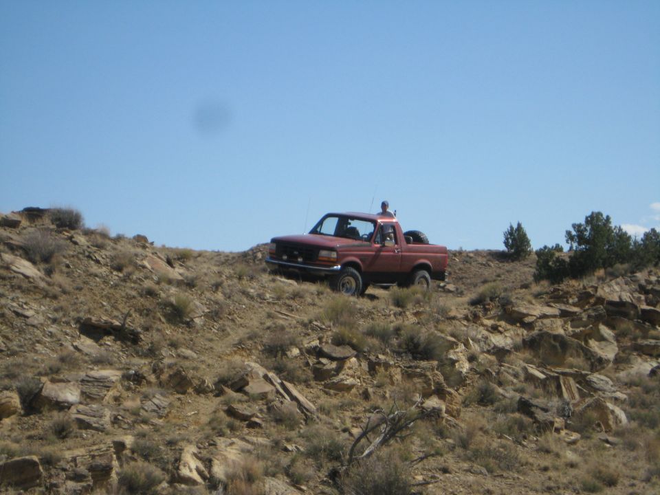 red pickup truck driving up a rocky, barren hill under a clear blue sky