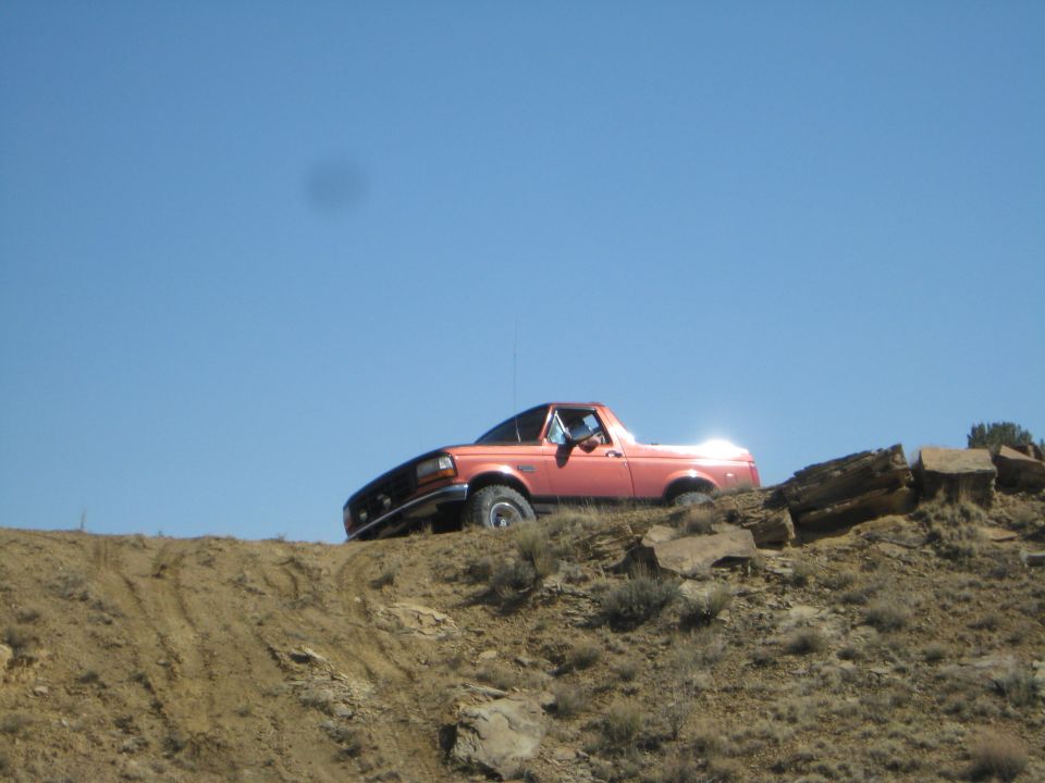 Orange 1993 Ford Bronco driving off-road on a dirt hill