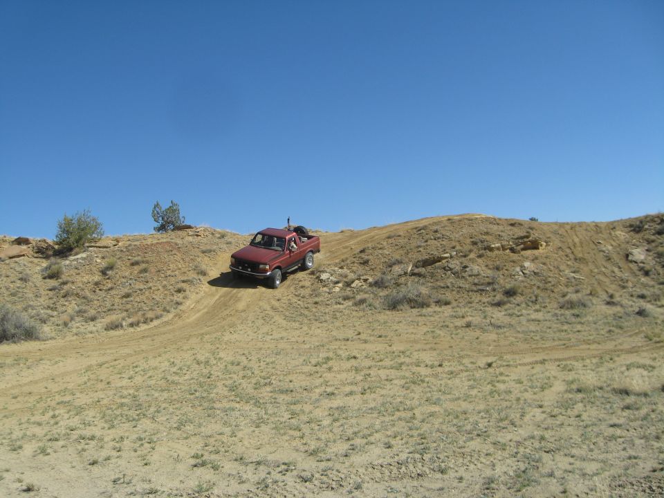 Red pickup truck driving up a dirt hill on a sunny day