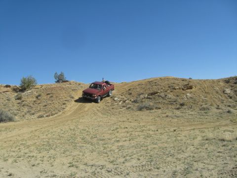 1993 Ford Bronco - Red pickup truck navigates a dirt track on a dry, hilly landscape.