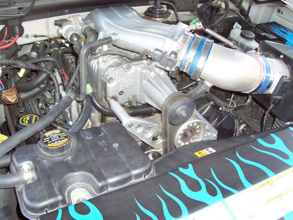 Close-up of a Ford engine with a supercharger and blue flame decals on a radiator cover