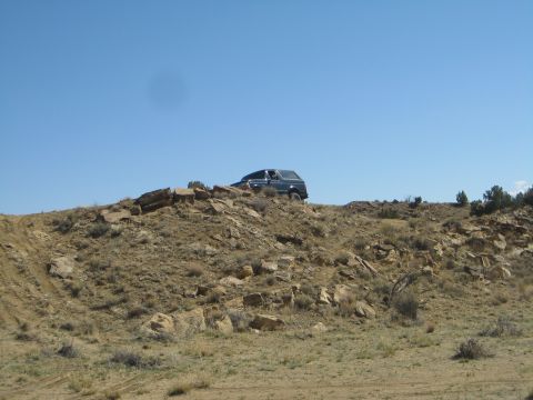 1993 Ford Bronco - A dark SUV navigates a rocky, arid terrain under a clear blue sky.