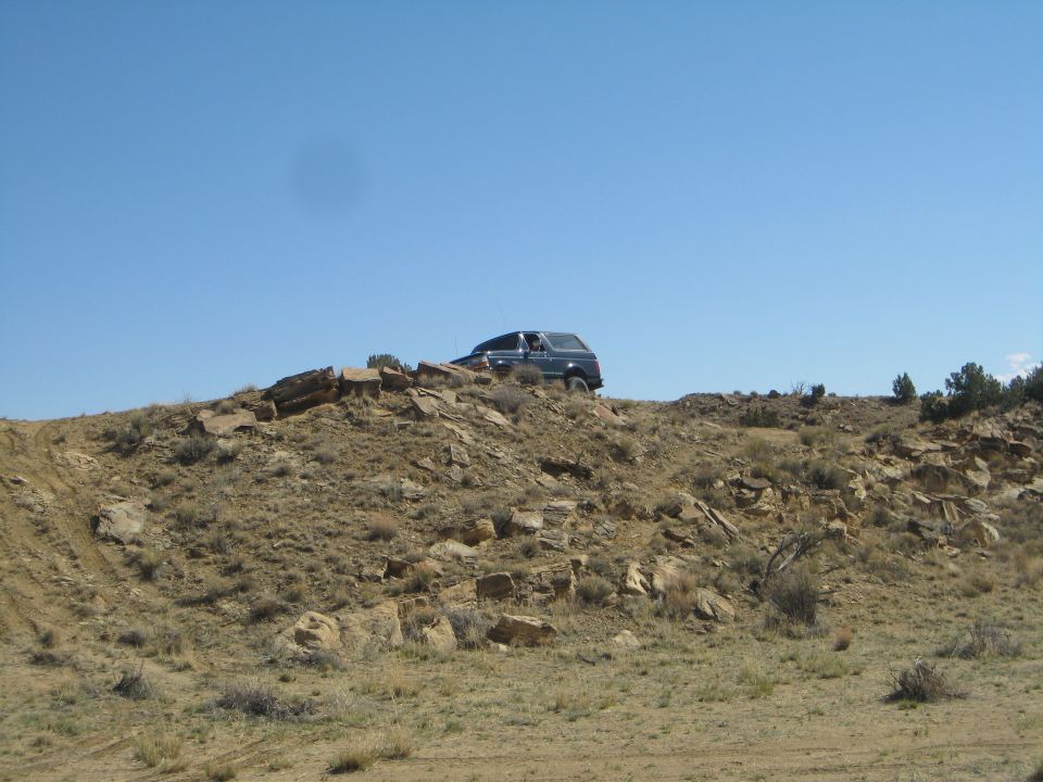 Dark SUV on rocky hill, front quarter view. Some dirt and brush visible